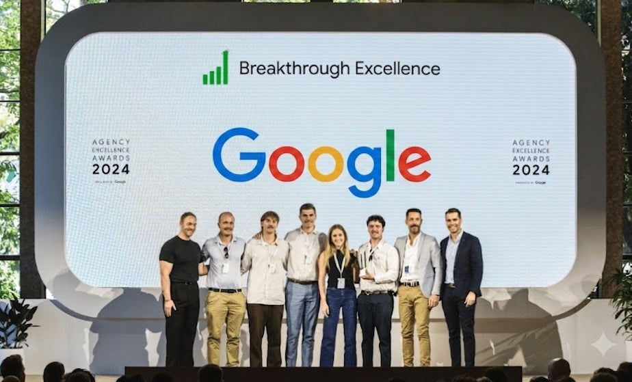 A group of eight people standing on a stage in front of a large screen displaying the Google Breakthrough Excellence 2024 logo and name.
